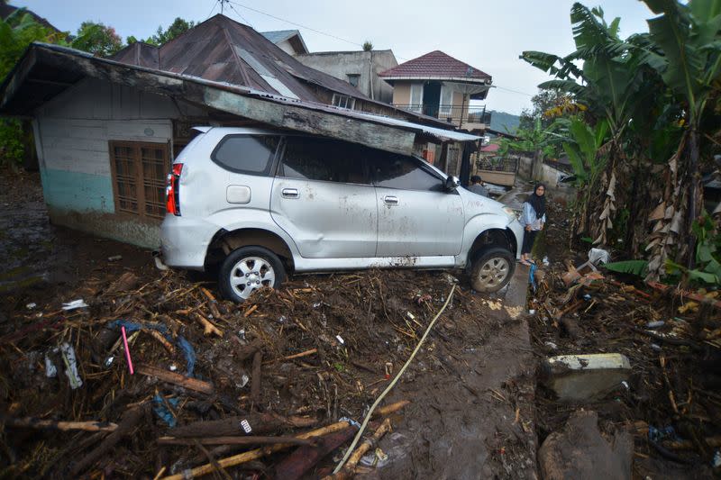 A woman stands near a damaged car in an area affected by heavy rain which caused flash floods in Agam