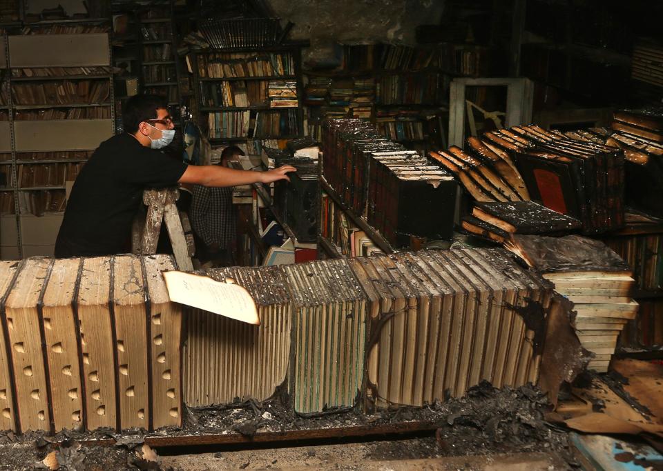 In this picture taken on Sunday, Jan. 5, 2014, a Lebanese activist removes burned books, at the Saeh (Tourist) Library which was set on fire by masked men, in the northern city of Tripoli, Lebanon. Books that were burnt in an arson attack targeting a crammed, chaotic and popular library in the northern Lebanese city of Tripoli have become the latest victim of the country's rising sectarian tensions. (AP Photo/Hussein Malla)