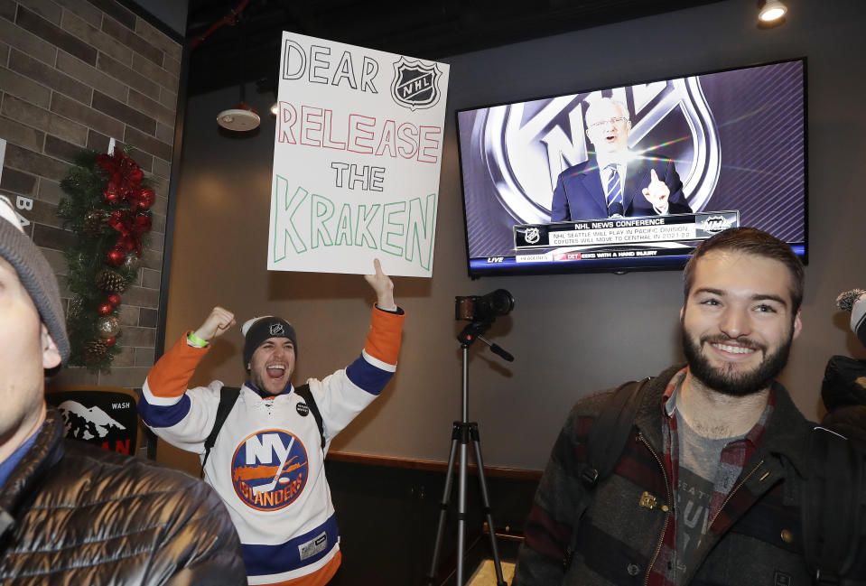 Max Rubin cheers and holds a sign in favor of the team name "Kraken" following the announcement of a new NHL hockey team in Seattle, at a celebratory party Tuesday, Dec. 4, 2018, in Seattle. (AP Photo/Elaine Thompson)