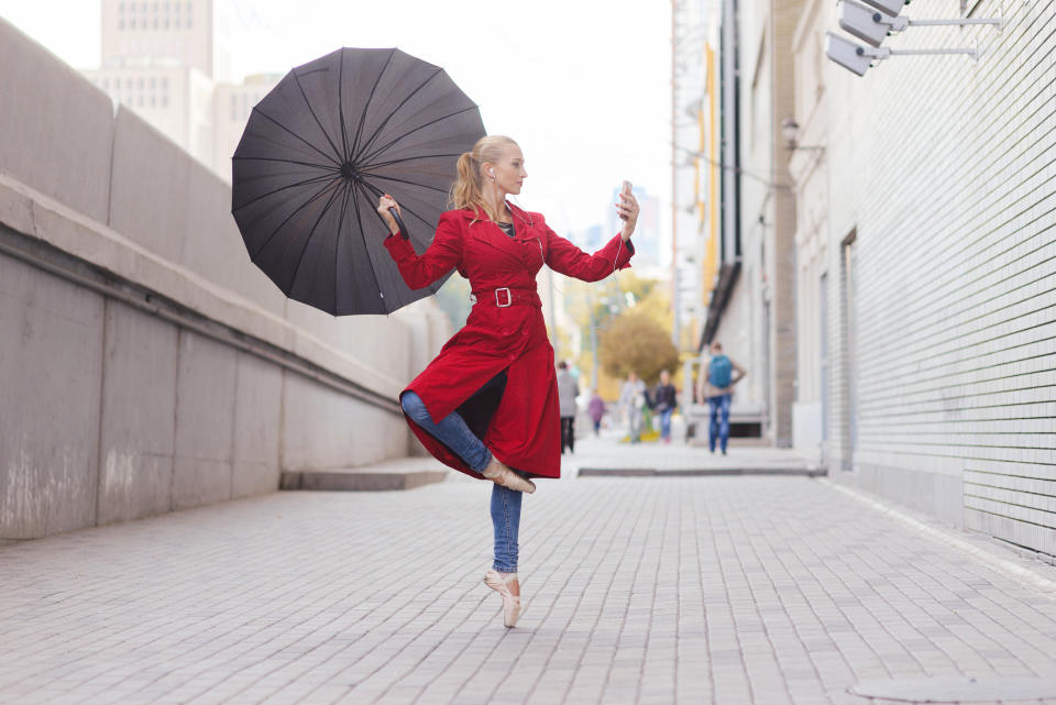 A young woman records herself dancing with an umbrella.