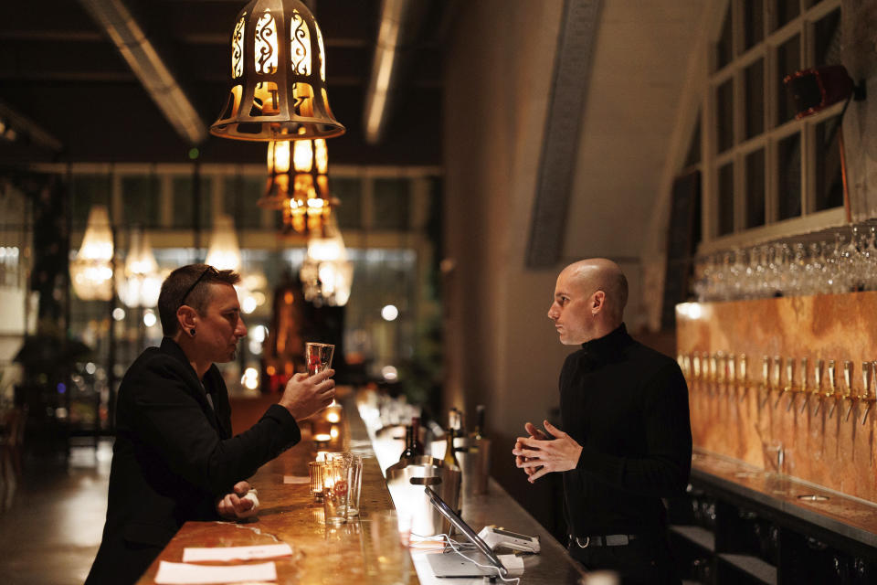 A man asks a bartender for a refill on his drink at Brasserie Surrealiste in Brussels, Wednesday, Sept. 28, 2022. A group of restaurant owners in Brussels has imagined how a future without gas and electricity would look like for gourmets. Dinner guests, served at the Brasserie Surrealiste and cooked by Racines restaurant employees, were the first to experience it: No ovens, no stoves, no hot plates, no coffee machines and no light bulbs. (AP Photo/Olivier Matthys)