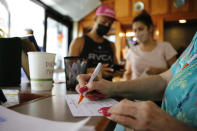 Highway Inn restaurant hostess Ku'uipo Lorenzo, right, records contact information for Martin Day, left, and his wife, Ashley Day, center, after they showed proof of vaccination and a negative COVID-19 test result on Monday, Oct. 25, 2021, in Honolulu. To comply with local mandates, the restaurant requires all indoor diners to show proof of vaccination or have a recent negative test result before being seated. (AP Photo/Caleb Jones)