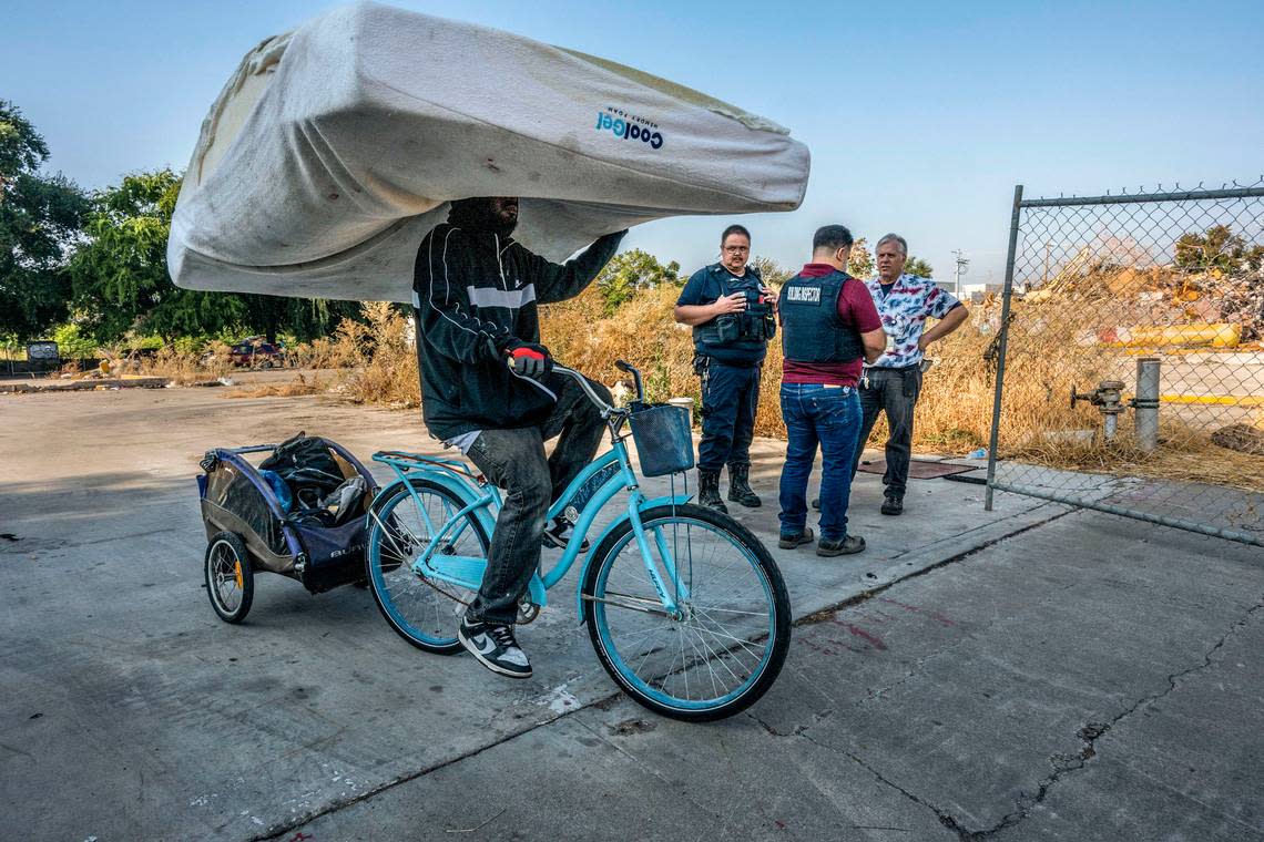 A homeless man carries a mattress as he cycles past city enforcement officers during a homeless encampment sweep on 1st Avenue in Sacramento in September.