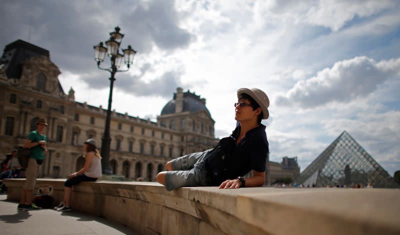 FILE PHOTO: A tourist sits in front of the Pyramid at the Louvre museum in Paris