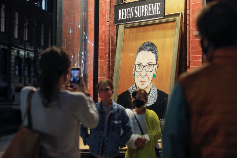 Children are photographed in front of a painting in a storefront on Broadway of Associate Justice of the Supreme Court of the United States Ruth Bader Ginsburg who passed away in Manhattan, New York City