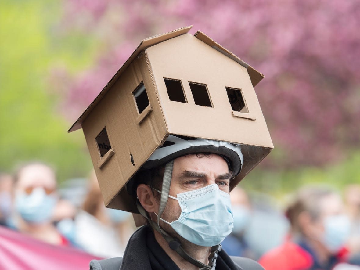 A man wears a cardboard house on his head during a demonstration calling for more affordable housing in Montreal last year. Private equity firms are now the biggest purchasers of homes in the U.S., worrying advocacy groups who say families can't compete against money managers with billions in assets.  (Graham Hughes/The Canadian Press - image credit)