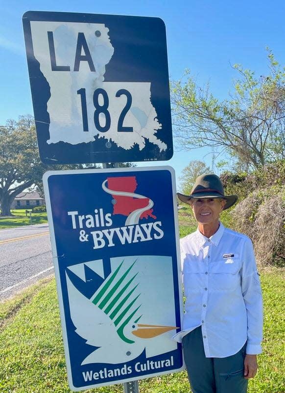 Edie Littlefield Sundby taking a photo by an LA 182 sign. Sundby is walking the Old Spanish Trail, a 2,750 mile path from the Atlantic to the Pacific Ocean. She began the journey in Texas, and is now passing through Terrebonne and Lafourche.