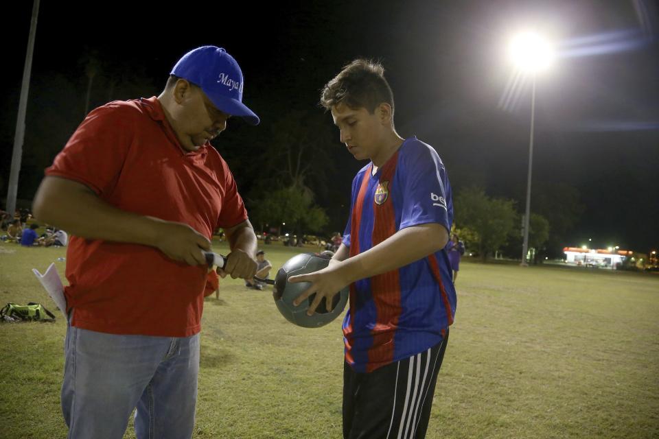 Antonio Velasquez, left, a pastor and director of the Maya Chapin soccer league of over 108 teams, helps inflate a soccer ball at a soccer league game Wednesday, April 17, 2019, in Phoenix. (AP Photo/Ross D. Franklin)