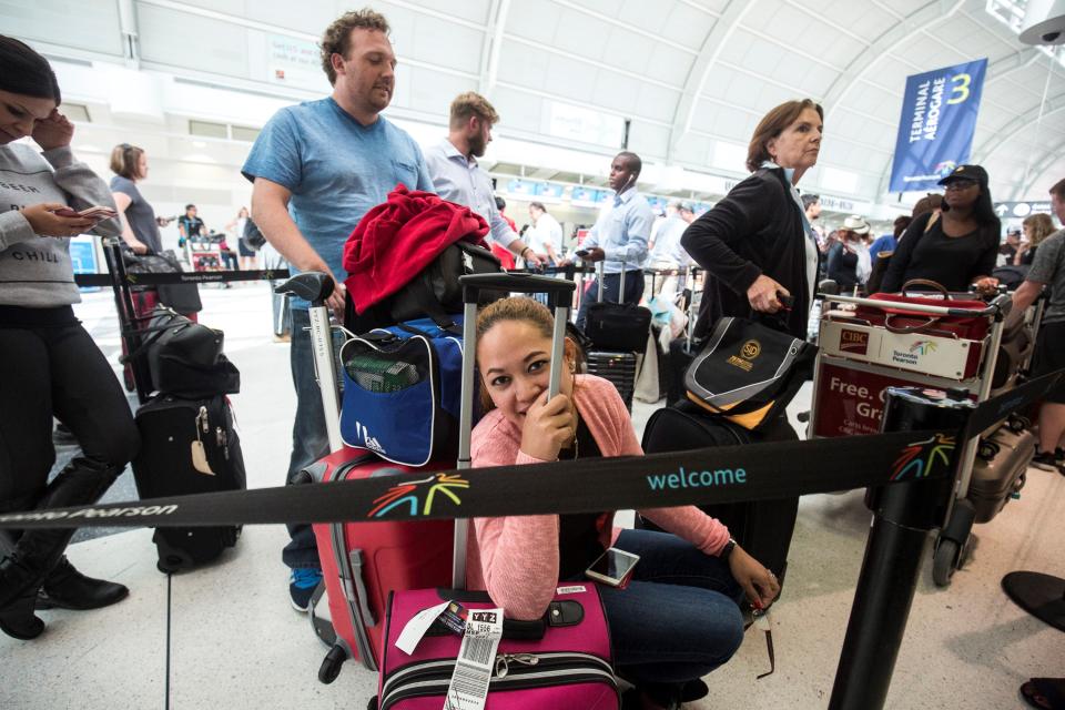 Milet McKeon, centre, uses her luggage as a seat as she waits in line at Pearson International airport, in Toronto, Canada on August 8, 2016. (Photo by Giordano Ciampini/Anadolu Agency/Getty Images)