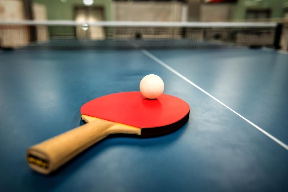 Ping pong on red racket, sitting on a ping pong table