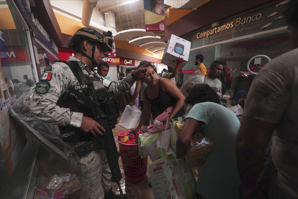 A Mexican National Guard soldier tries to stop people carrying away items like diapers and canned items from a store at a shopping mall, and others taking electronics after Hurricane Otis ripped through Acapulco, Mexico, Wednesday, Oct. 25, 2023. Hurricane Otis ripped through Mexico's southern Pacific coast as a powerful Category 5 storm, unleashing massive flooding, ravaging roads and leaving large swaths of the southwestern state of Guerrero without power or cellphone service. (AP Photo/Marco Ugarte)