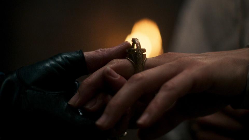 An extreme close-up shot of Moiraine’s gloved hand holding Lady Amalisa’s (Sandra Yi Sencindiver). Amalisa wears the golden Great Serpent ring of the Aes Sedai, but the colored gem denoting Ajah is missing