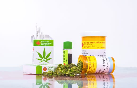 An assortment of legal Canadian cannabis products on a counter, with one prescription bottle on its side with cannabis buds spilling out of it .
