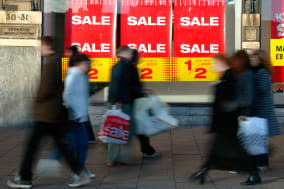 AR3A35 Sale signs in window of High Street store with moving shoppers carrying bags in foreground