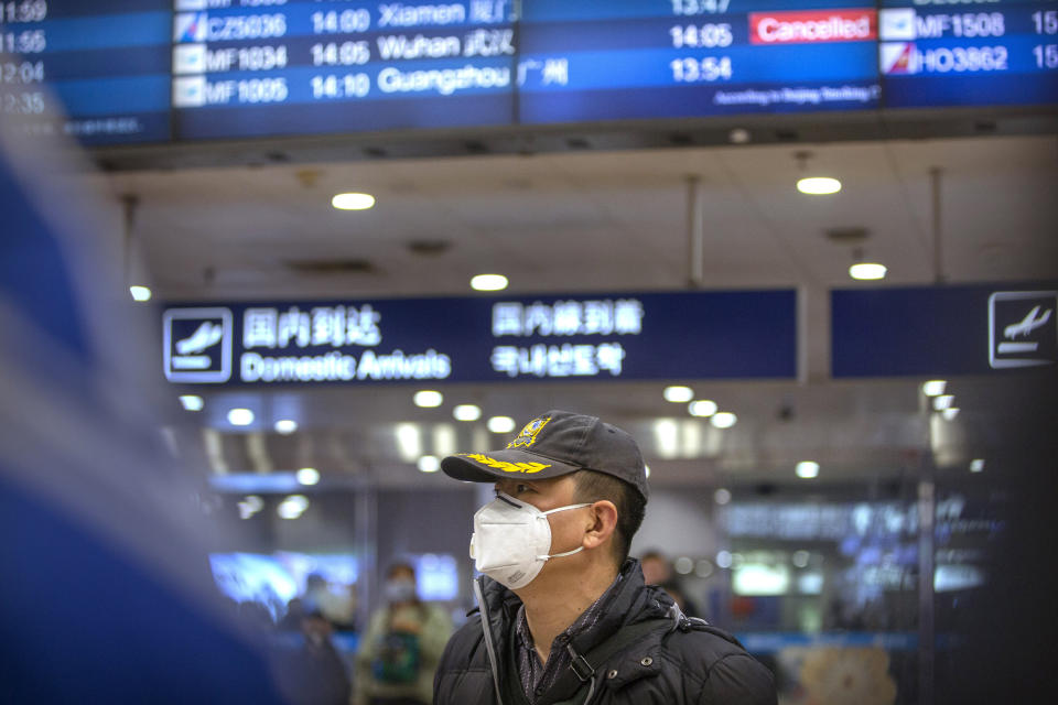 A traveler wears a face mask beneath an information display showing a canceled flight from Wuhan at Beijing Capital International Airport in Beijing, Thursday, Jan. 23, 2020. China closed off a city of more than 11 million people Thursday, halting transportation and warning against public gatherings, to try to stop the spread of a deadly new virus that has sickened hundreds and spread to other cities and countries in the Lunar New Year travel rush. (AP Photo/Mark Schiefelbein)