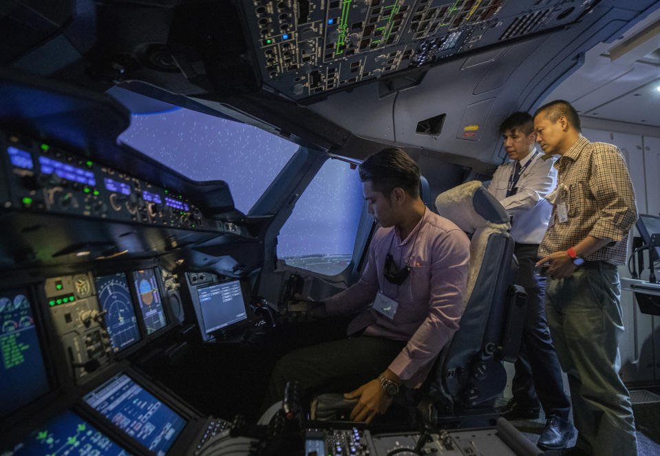 Pilot Akarapol Apanant, center, explains to customers in a Boeing A380 flight simulator at the Thai Airways head office in Bangkok, Thailand on Oct. 3, 2020. The airline is selling time on its flight simulators to wannabe pilots while its catering division is serving meals in a flight-themed restaurant complete with airline seats and attentive cabin crew. The airline is trying to boost staff morale, polish its image and bring in a few pennies, even as it juggles preparing to resume international flights while devising a business reorganization plan. (AP Photo/Sakchai Lalit)