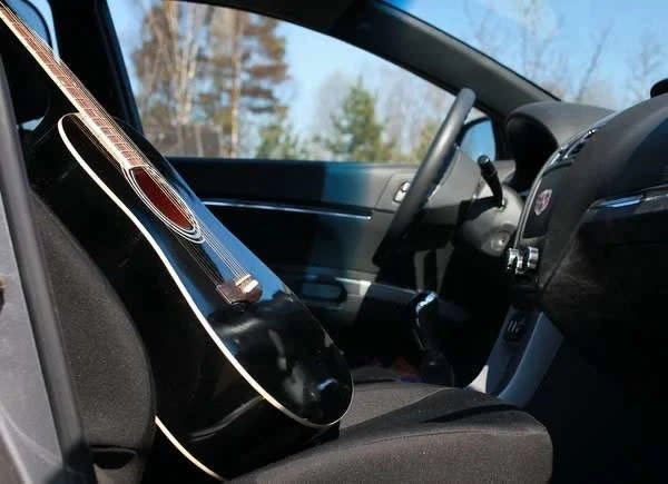 Black acoustic guitar on the front passenger seat of a car.