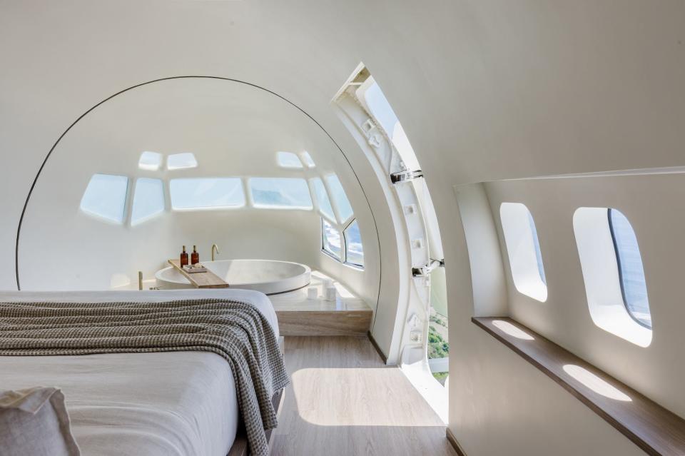 A bed overlooks a jacuzzi built into a bedroom. Windows fill the round area.