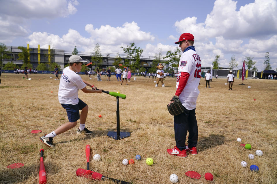 A kid hits a baseball during the MLB First Pitch Festival, as former MLB player David Eckstein looks at the Queen Elizabeth Olympic Park, in London, Thursday, June 22, 2023. Britain's relative success at the World Baseball Classic and the upcoming series between the Chicago Cubs and St. Louis Cardinals has increased London's interest about baseball. The sport's governing body says it has seen an uptick in interest among kids. (AP Photo/Alberto Pezzali)