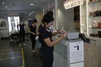 Salon owner Sian Rose Maclaren, right, sticks a label on a box that will house masks clients can buy if they don't already have one, as they prepare to reopen at a franchise branch of the Headmasters group of hairdressing salons, in Surbiton, south west London, Thursday, July 2, 2020. Millions of people in Britain will be able to go to the pub, visit a movie theater, get a haircut or attend a religious service starting July 4, in a major loosening of coronavirus lockdown restrictions. (AP Photo/Matt Dunham)