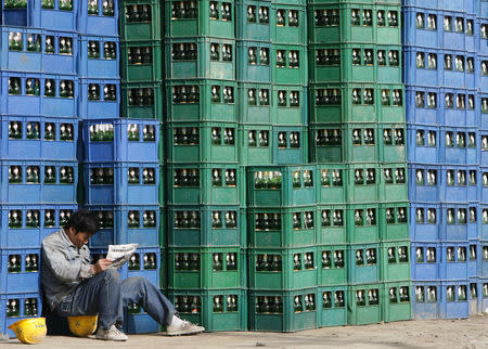 A migrant worker reads a newspaper beside cases of beer in Beijing November 2, 2007. REUTERS/Claro Cortes/Files