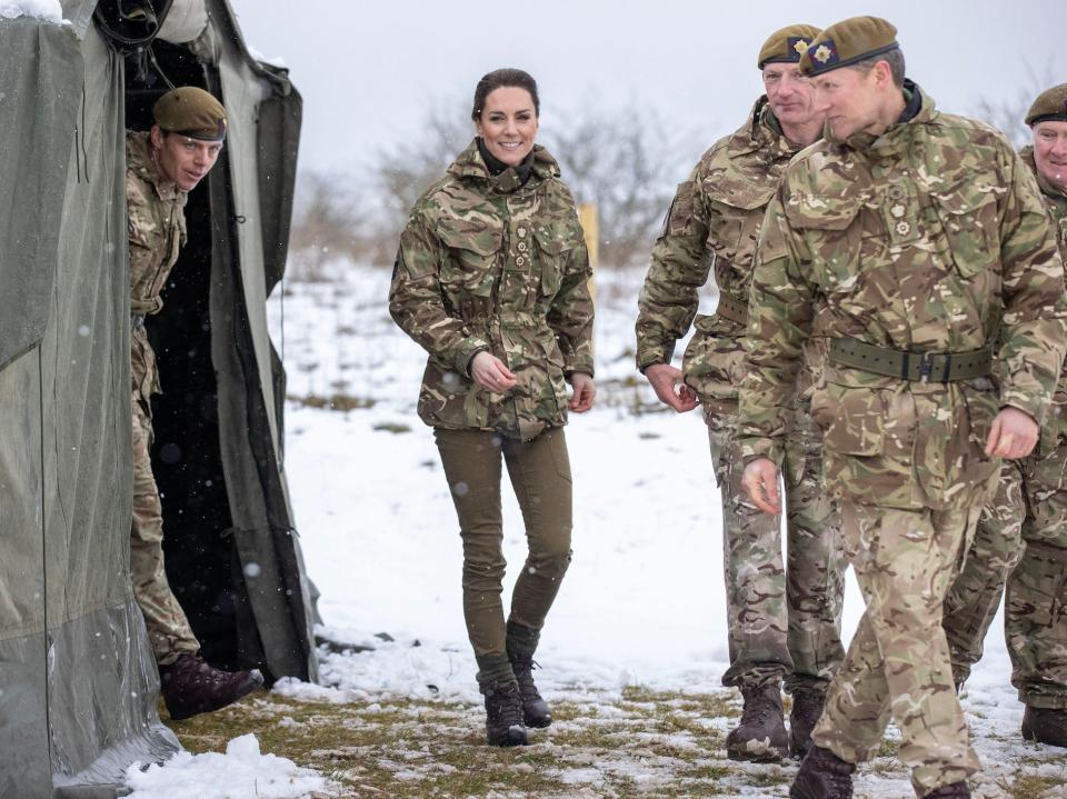 Kate Middleton wears camouflage and walks with other soldiers in a snowy environment.