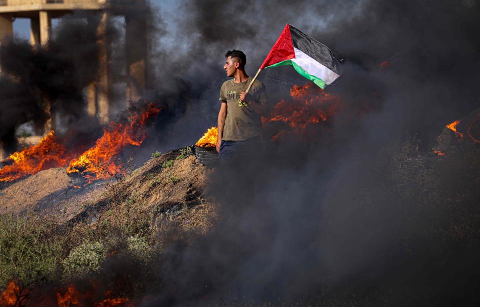 A Palestinian youth holds a flag next to burning tires during a protest by the border fence with Israel east of Gaza City on July 3, 2023. Israel has stepped up operations in the northern West Bank, home to Jenin city and its adjacent refugee camp, a stronghold of Palestinian armed groups where there has been a spate of attacks on Israelis as well as attacks by Jewish settlers on Palestinian communities. (Photo by MAHMUD HAMS / AFP)