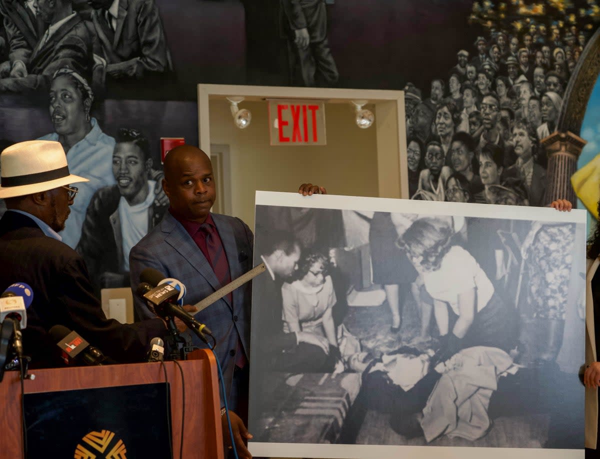 Mustafa Hassan points to a photo of himself next to Malcolm X after he was shot (Ariana Baio / The Independent)