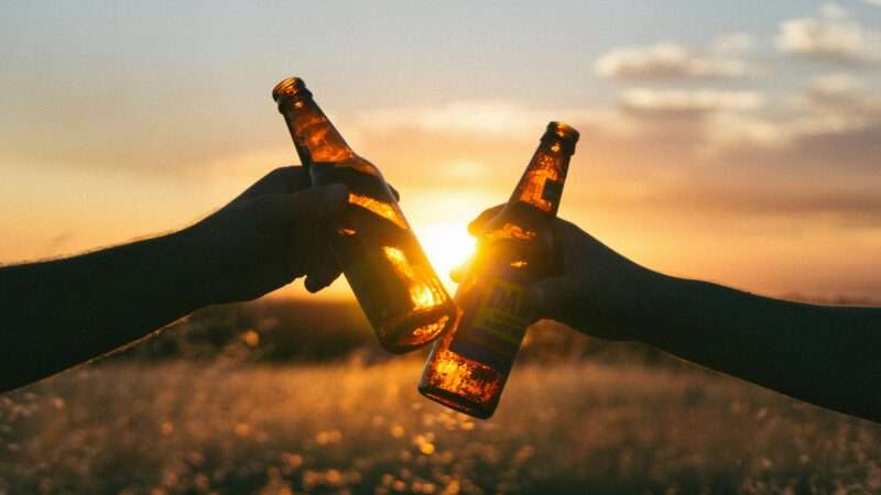 Two people clinking their beers at sunset