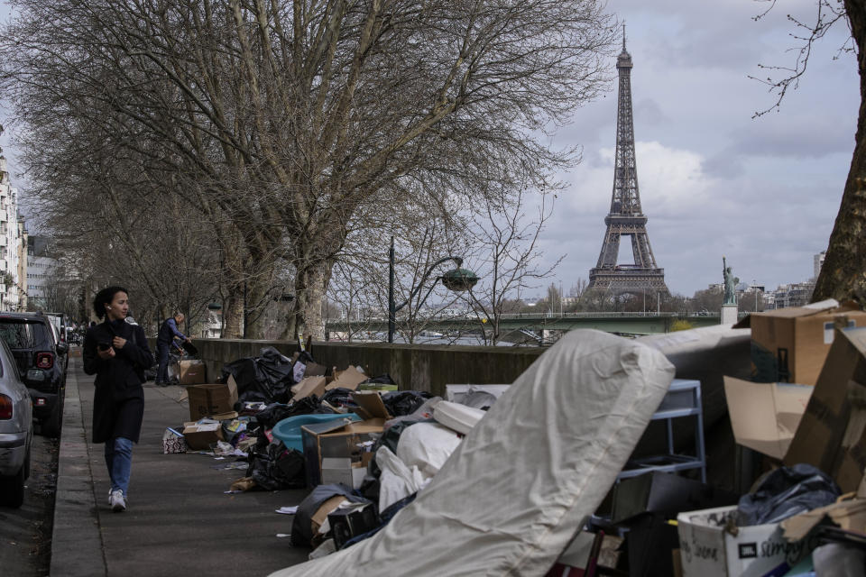 A woman walks past uncollected garbages in Paris, Thursday, march 23, 2023. French unions are holding their first mass demonstrations Thursday since President Emmanuel Macron enflamed public anger by forcing a higher retirement age through parliament without a vote. Eiffel Tower in the background. (AP Photo/Christophe Ena)