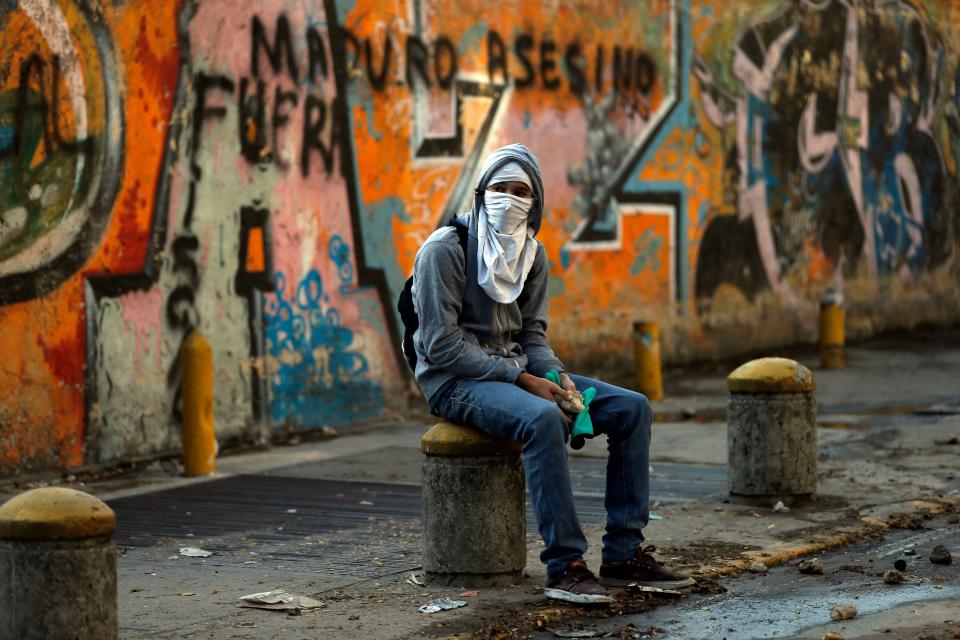 A demonstrators takes a break from the confrontations with police, next to graffiti written on a wall that reads in Spanish "Maduro killer, out", during anti-government protests in Caracas, Venezuela, Tuesday, March 4, 2014. After almost a year after the death of Hugo Chavez, Venezuela has been rocked by weeks of violent protests that the government says have left 18 dead. President Maduro appears ready to use Chavez's almost mythical status to steady his rule as protesters refuse to leave the streets. (AP Photo/Fernando Llano)