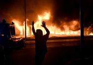 Un hombre camina al lado de un vehículo blindado mientras B&L Office Furniture se quema en el fondo después de protestas que terminaron en incendios luego de que la policía disparó varias veces a un hombre negro, identificado como Jacob Blake, anoche en Kenosha, Wisconsin, Estados Unidos.