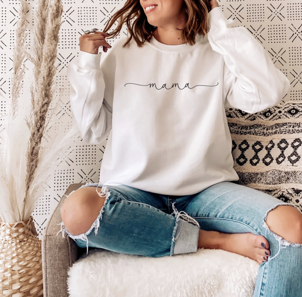 woman wearing Mama Sweatshirt in white with blue ripped jeans (Photo via Etsy)