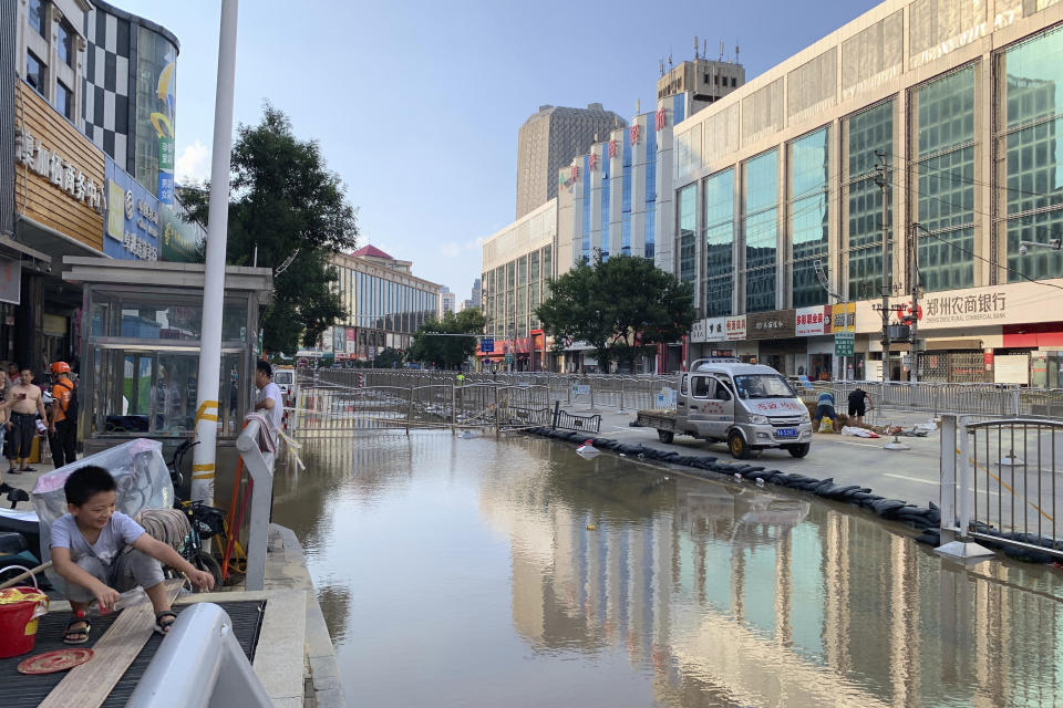 A child squats next to a flooded road in the aftermath of the heaviest recorded rainfall in Zhengzhou in central China's Henan province on Saturday, July 24, 2021. Rescuers used bulldozers and rubber boats to move residents out of flooded neighborhoods in central China on Saturday after torrential rains killed at least 56 people. (AP Photo/Dake Kang)