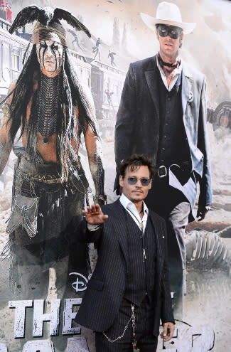 Johnny Depp waves to fans as he walks a red carpet in front of a giant screen graphic of his film "The Lone Ranger."