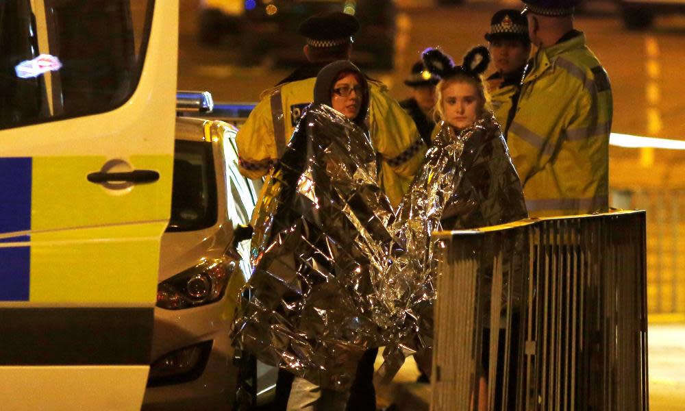 Two women wrapped in thermal blankets stand near the Manchester Arena, where a terror attack took place after a performance by Ariana Grande.