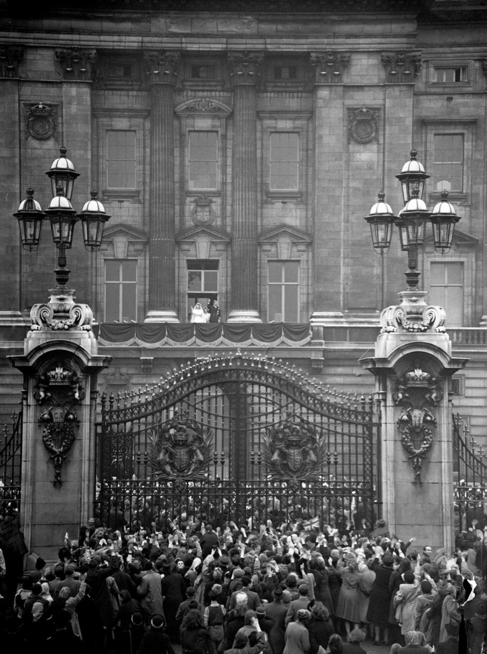 The Bride and Groom wave from the balcony as crowds gather at the gates of Buckingham Palace to greet the happy couple (PA )