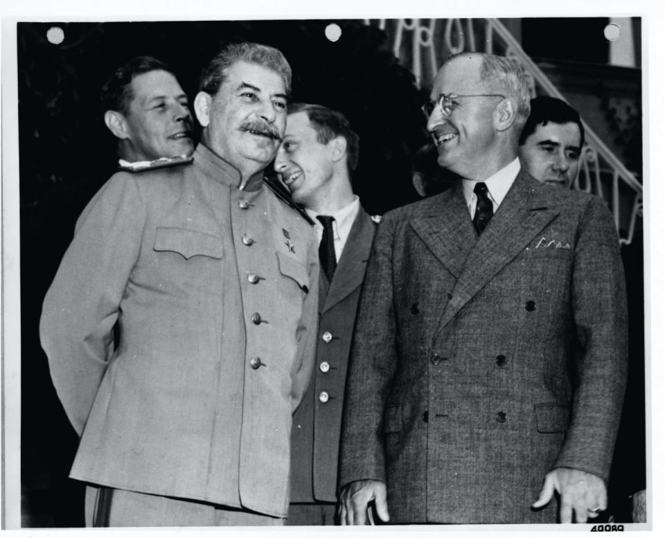 A man in a military uniform stands next to a man dressed in a business suit and both are smiling.