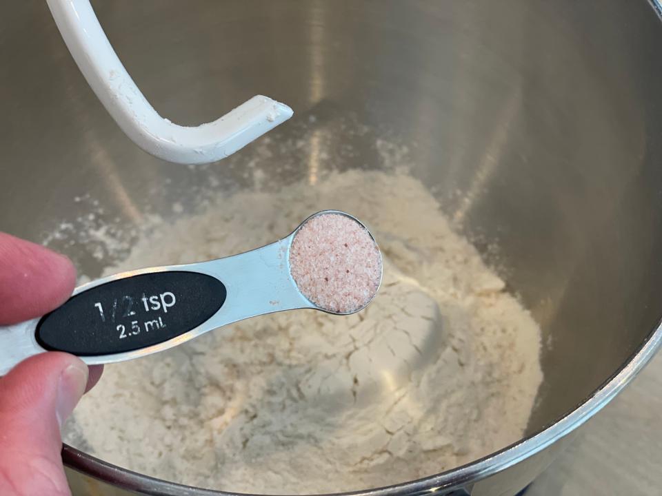 hand pouring a teaspoon of salt into a mixing bowl with flour