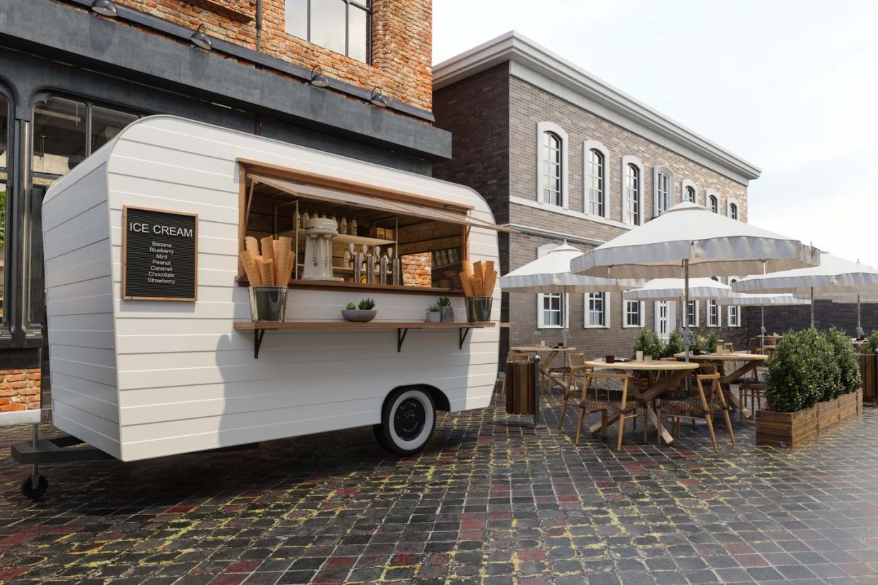 close up view of ice cream van with wooden tables, chairs and parasols