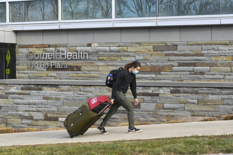 Cornell University sophomore, Kieran Adams, wheels his luggage through the university's campus in Ithaca, N.Y., Thursday, Dec. 16, 2021, en route to go home. Facing rising infections and a new COVID-19 variant, colleges across the U.S. have once again been thwarted in seeking a move to normalcy and are starting to require booster shots, extend mask mandates, limit social gatherings and, in some cases, revert to online classes. Cornell University abruptly shut down all campus activities on Tuesday and moved final exams online after more than 700 students tested positive over three days. (AP Photo/Heather Ainsworth)