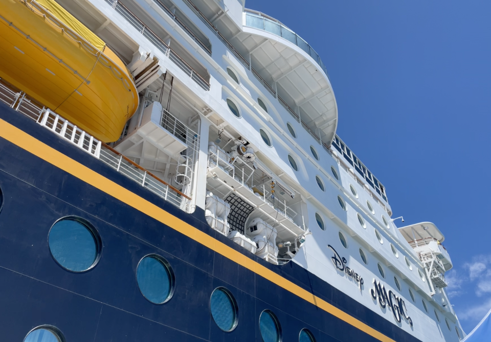 Side view of a Disney cruise ship with round windows in the hull, multiple decks, and a water slide