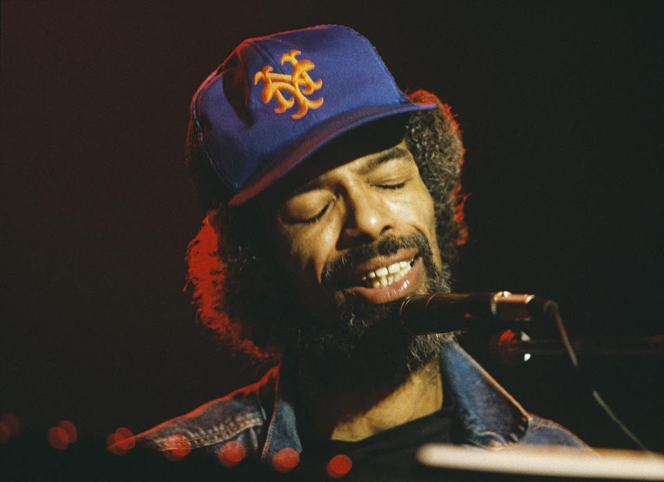 A Black man in a baseball cap performing at a piano