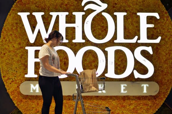 A person pushing a shopping cart in front of a Whole Foods Market sign.