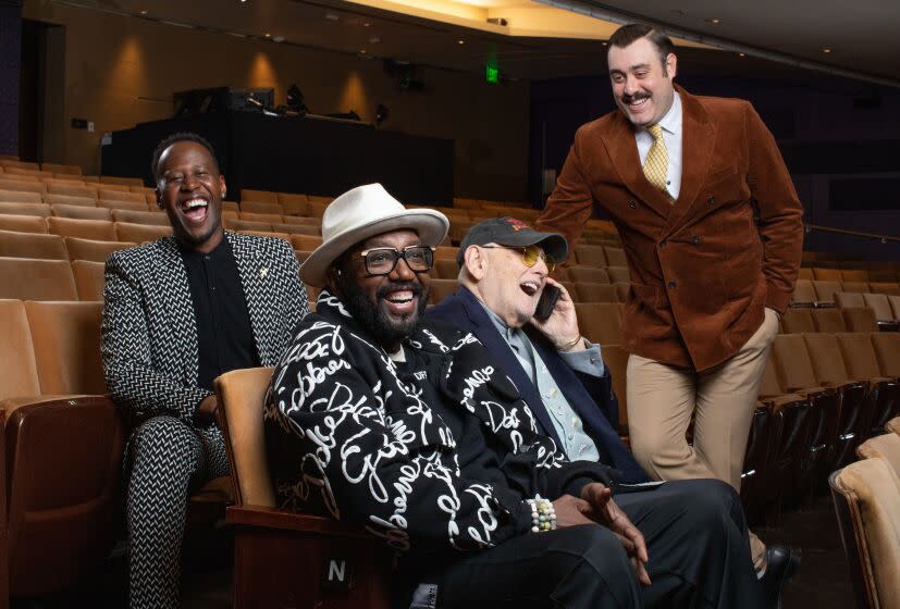 Four men are in the seats of an auditorium laughing