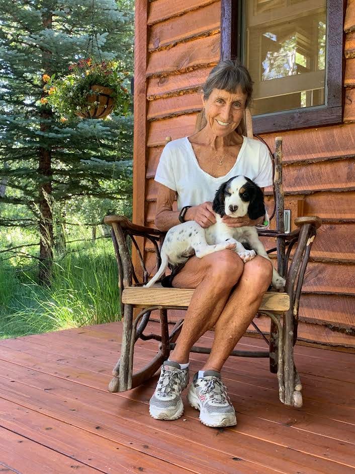Herald-Tribune columnist Carrie Seidman is pictured on the porch of a guest cabin owned by her sister, Meg, and brother in law, Hal Williams in Red Lodge, Montana. Seidman, holding the Williamses'  two-month-old English setter puppy, Razz, is recuperating from a major health scare that occurred during her vacation in Montana.