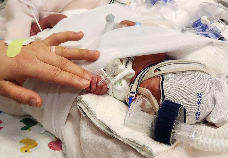 Mercedes Sandhu uses her finger to hold the hand of one of her newborn quadruplets at Texas Children's Hospital.