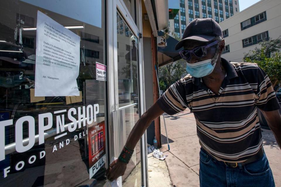 A man wears a mask as he cleans the outside of the StopnShop food and deli store in Miami on Tuesday.