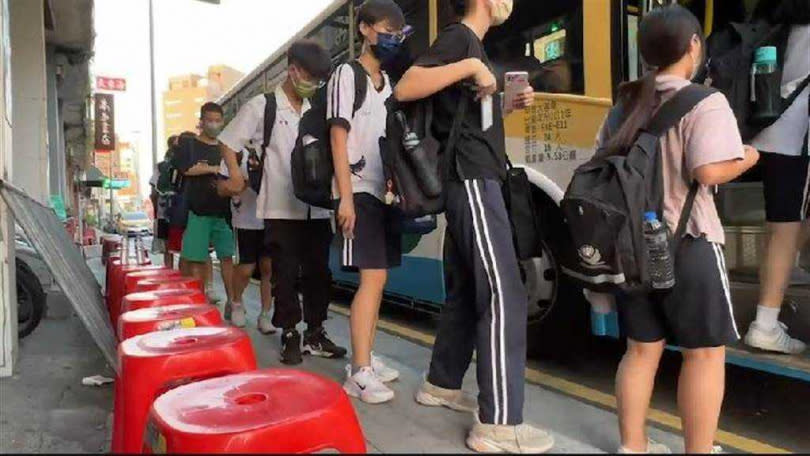 彰化火車站前「學生等候公車」擠在騎樓席地而坐，熱心人送紅色塑膠椅給學生坐。（圖／民眾提供）