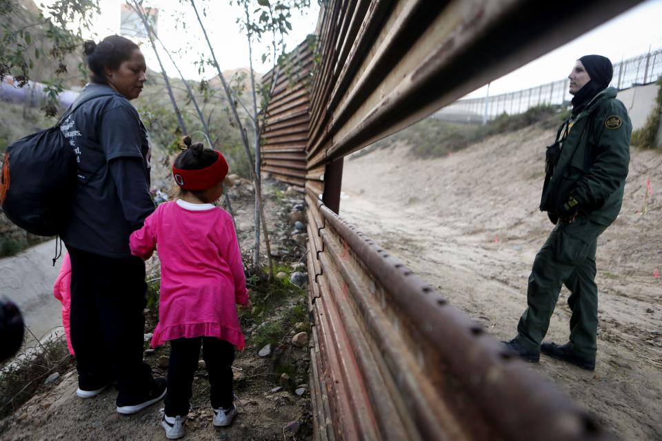 A Honduran mother and daughter, part of a caravan of thousands attempting to reach the U.S., stand next to a hole in the U.S.-Mexico border fence after speaking to a U.S. Border Patrol agent on the other side on Dec. 15, 2018, in Tijuana, Mexico.